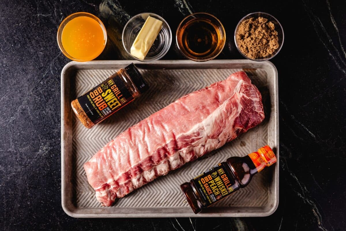 An overhead shot on pork ribs on a baking sheet with a jar of BBQ sauce and a bottle of BBQ rub.