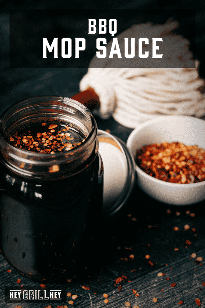 Mop sauce in a glass mason jar next to a sauce mop and a bowl of red pepper flakes with text overlay - BBQ Mop Sauce.