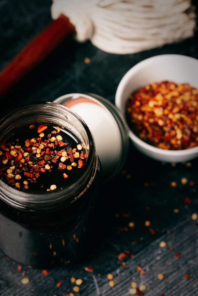 Mop sauce in a glass mason jar next to a sauce mop and a bowl of red pepper flakes.
