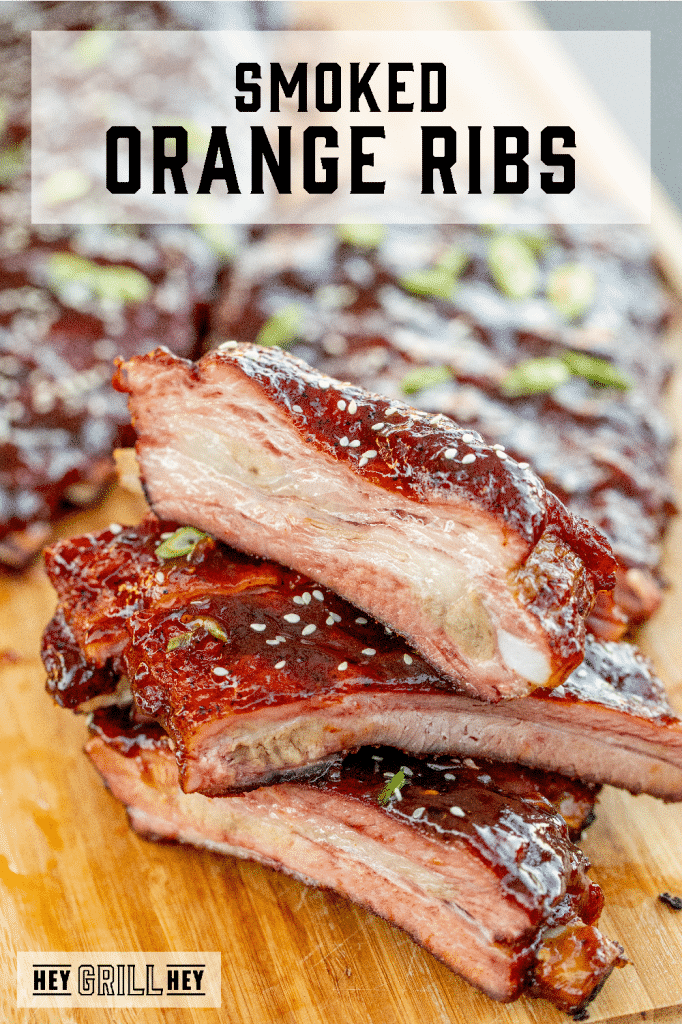 Sliced and stacked orange glazed ribs on a wooden cutting board with text overlay - Smoked Orange Ribs.