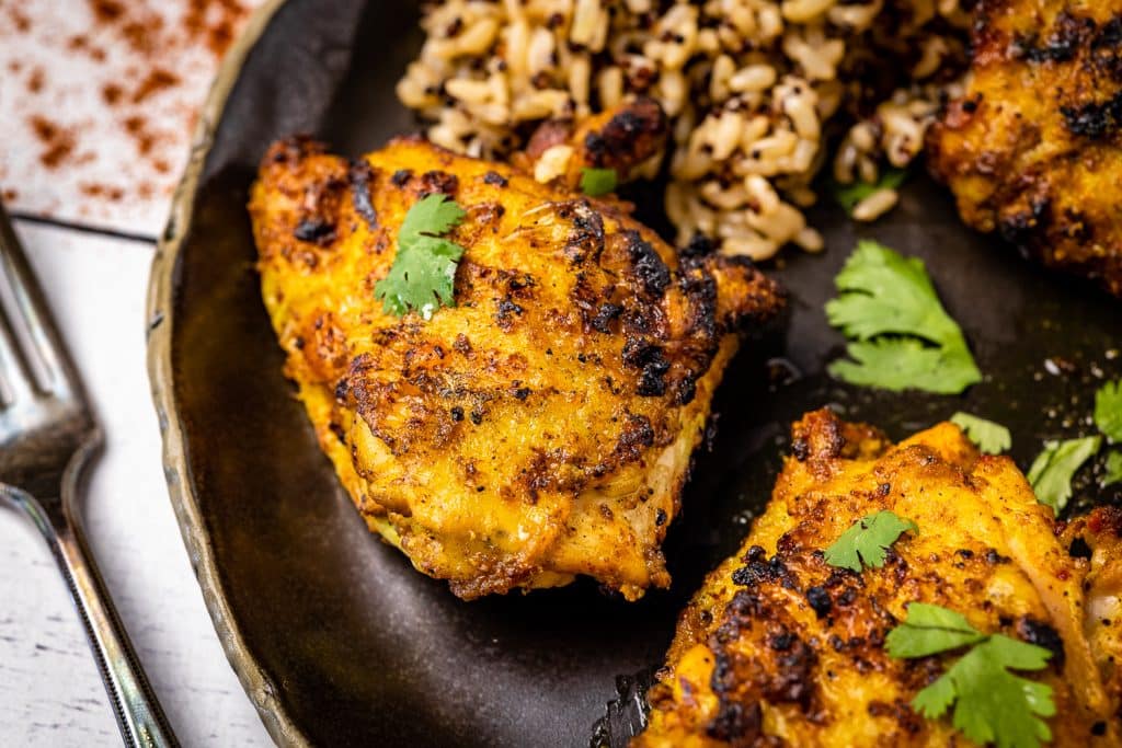 Tandoori chicken thighs on a plate next to rice and a fork.