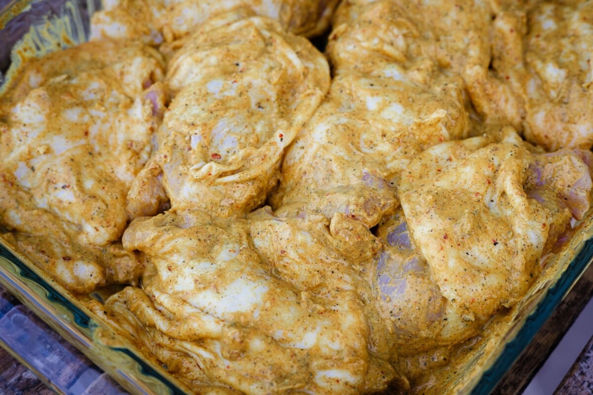 Chicken thighs in a tandoori marinade in a glass baking dish.