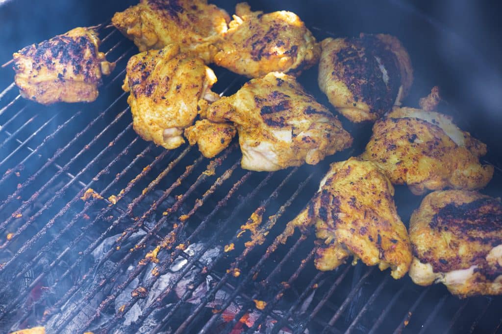 Tandoori chicken on the grill with smoke rising from below the grates.