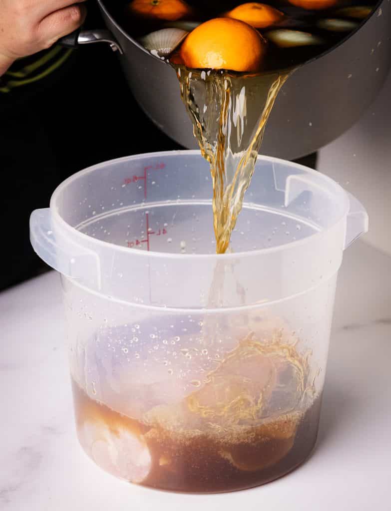 Brine being poured over a turkey breast in a large plastic container.