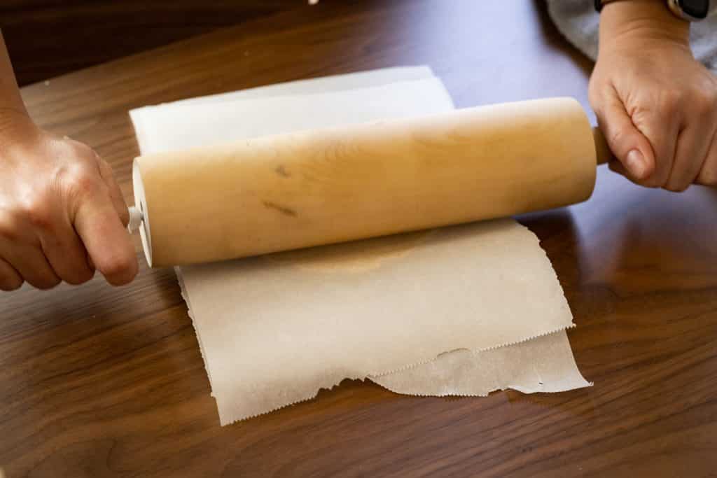 Corn tortilla being rolled between two pieces of parchment paper.