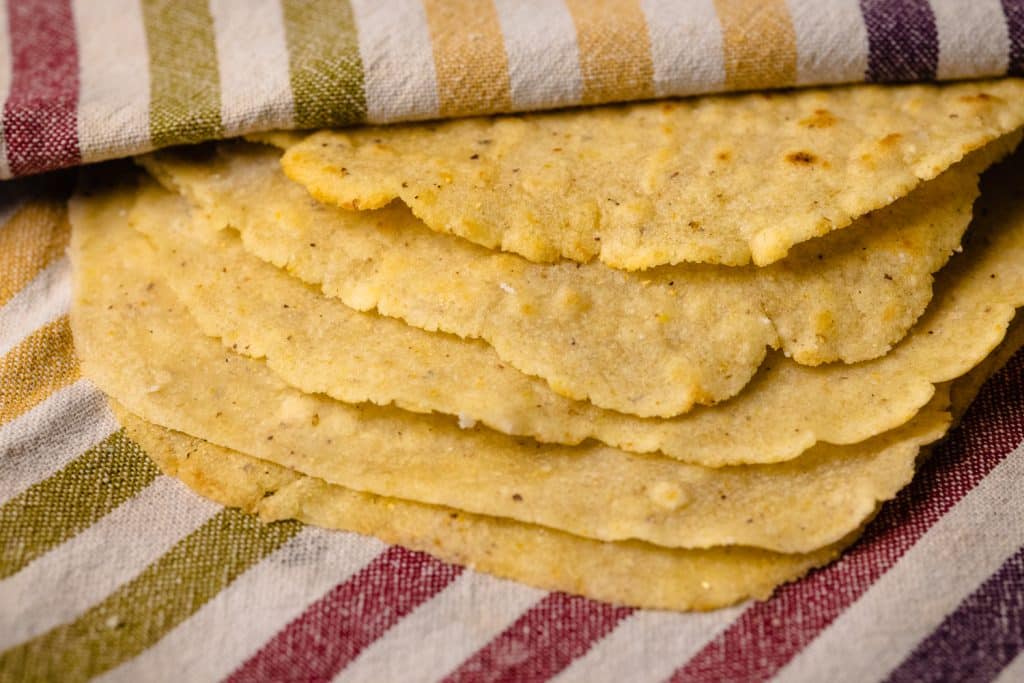 Stack of grilled corn tortillas on a kitchen towel.