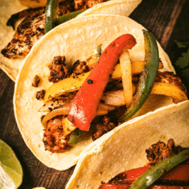 Three grilled chicken fajitas on a wooden serving board.