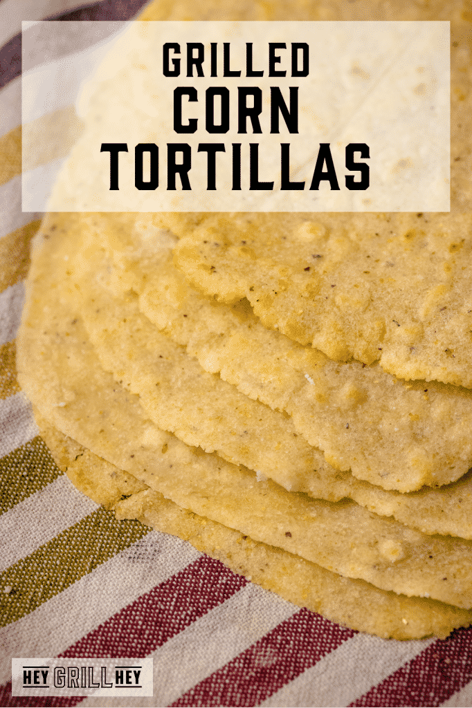 Stack of grilled corn tortillas on a kitchen towel with text overlay - Grilled Corn Tortillas.