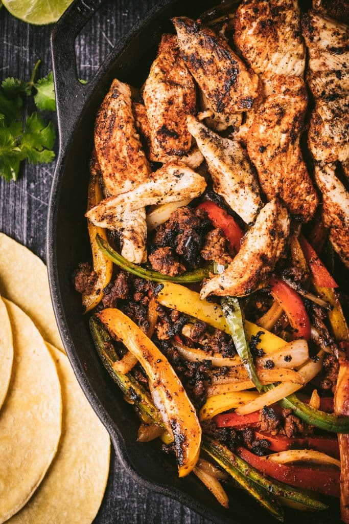 Chicken and peppers in a cast iron skillet next to corn tortillas.