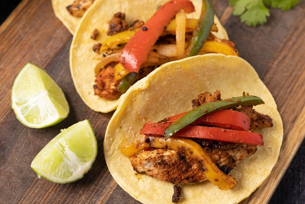 Three grilled chicken fajitas on a wooden serving board.