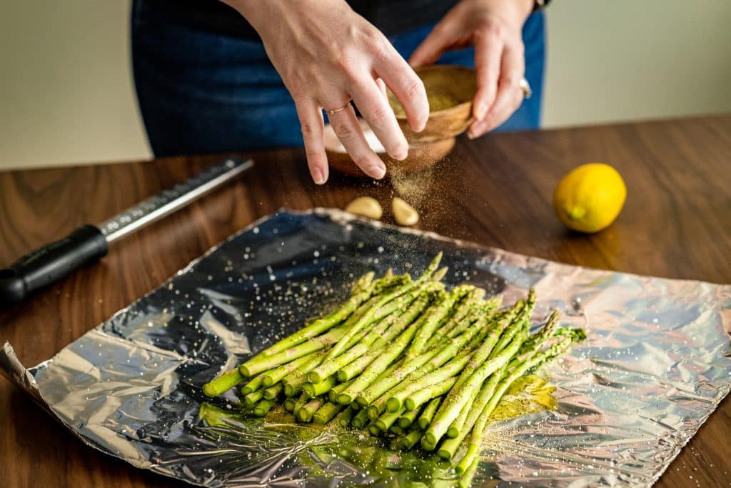 Salt and pepper being sprinkled on a pile of asparagus.