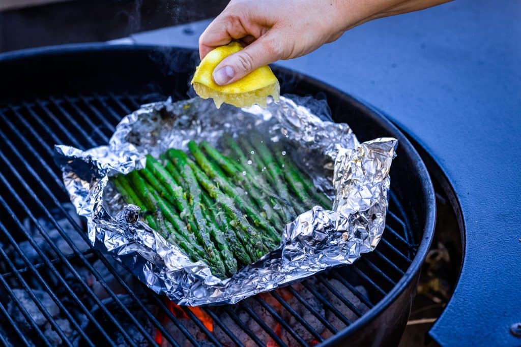 Fresh lemon being squeezed over grilled asparagus in foil.