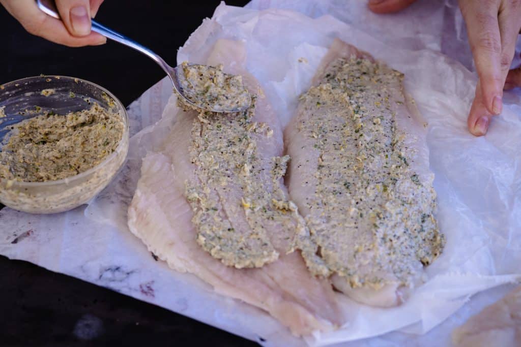Seasoning paste being spread on two catfish filets.
