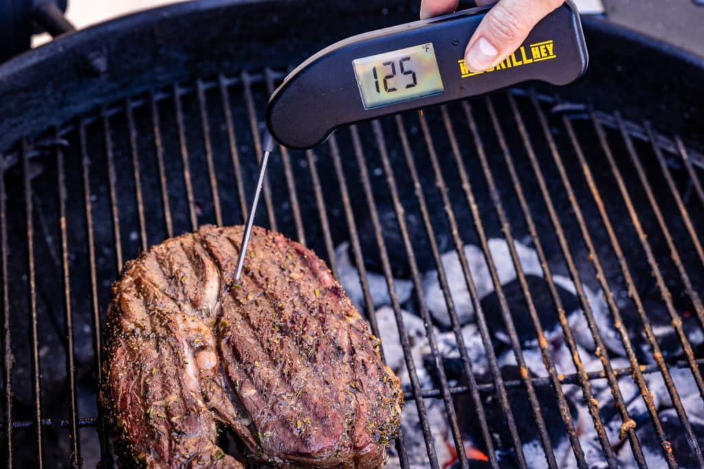 Instant read thermometer measuring temperature of a leg of lamb on the grill at 125 degrees F.