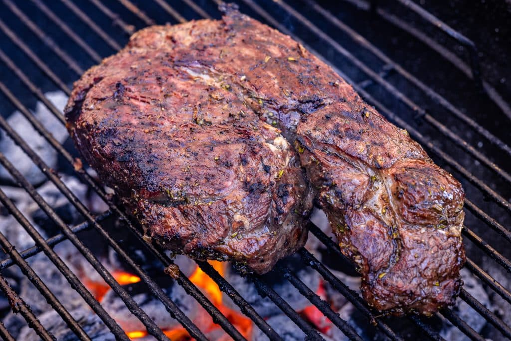 Grilled leg of lamb on grill grates over hot coals.