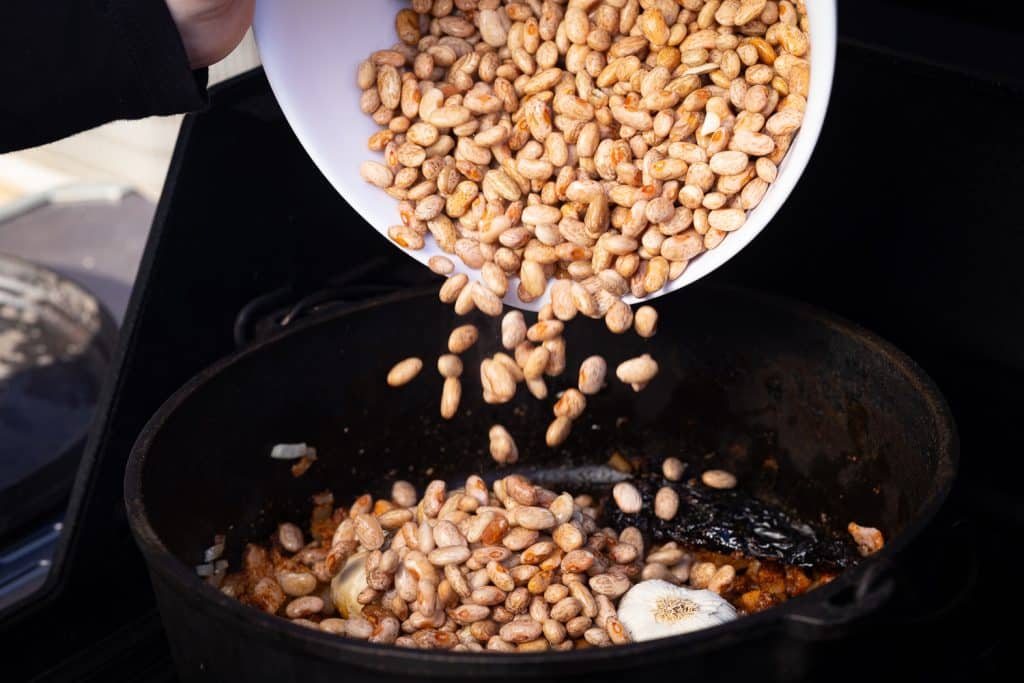 Beans being poured into a skillet of seasonings.