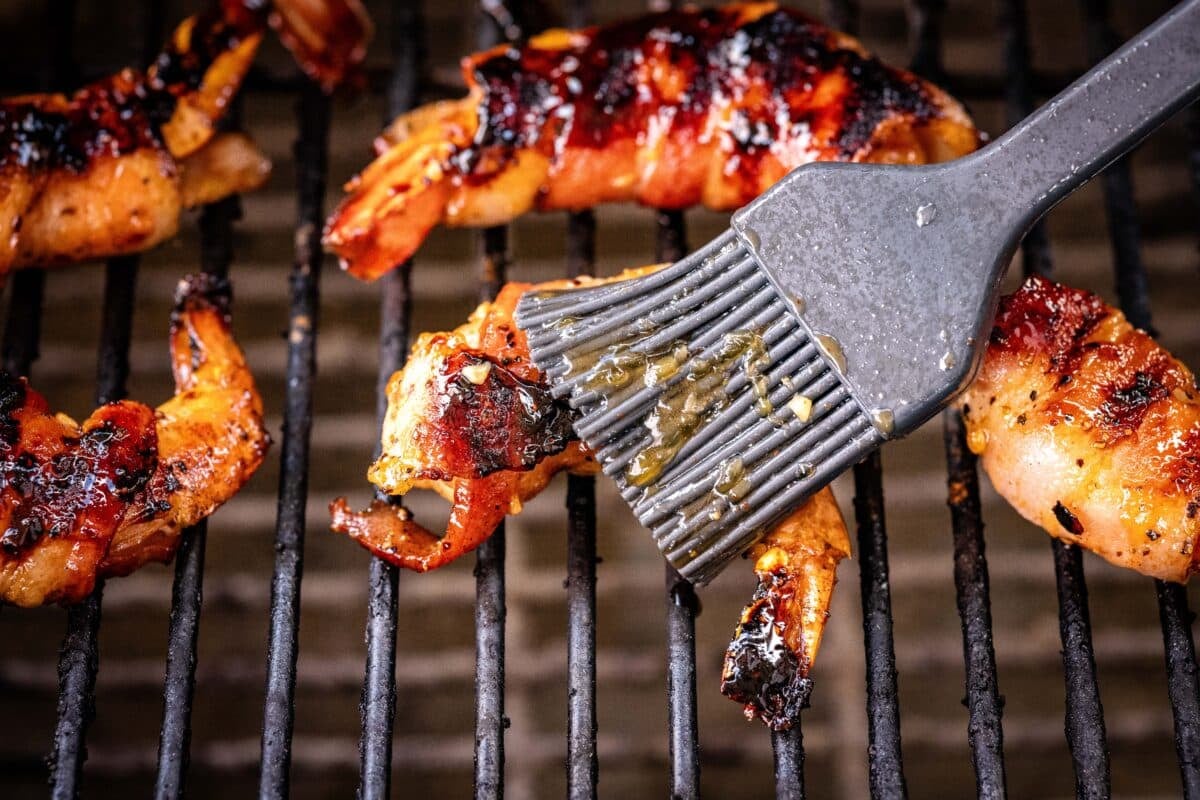 A rubber brush slathering sauce onto food on grill grates.