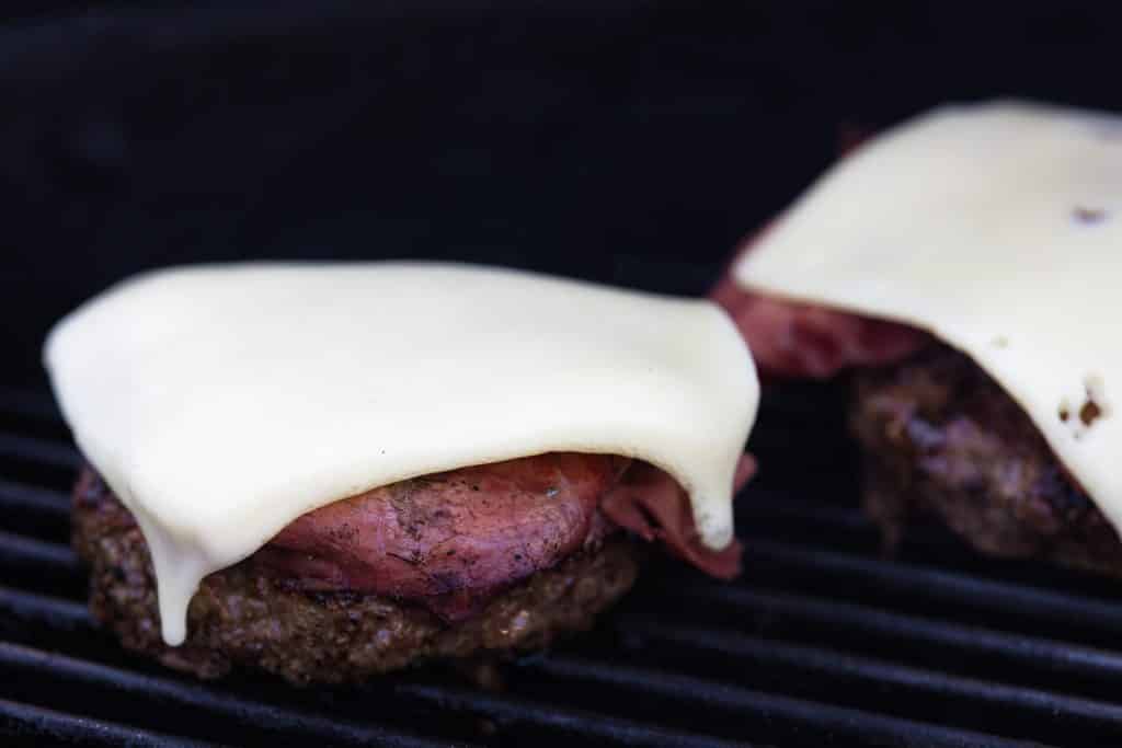 Swiss cheese melting on a beef burger on the grill.