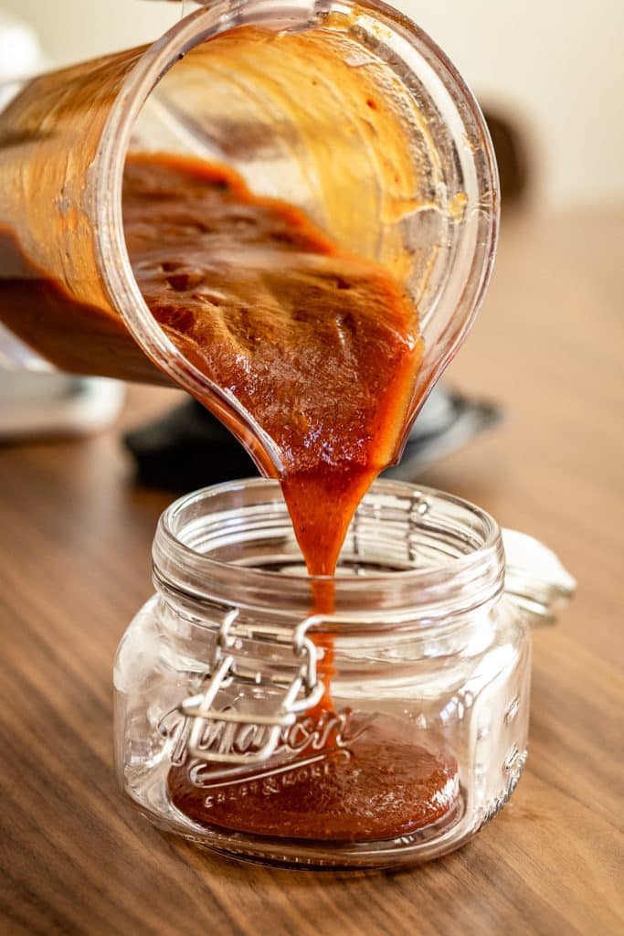 Honey chipotle BBQ sauce being poured into a hinged glass mason jar.