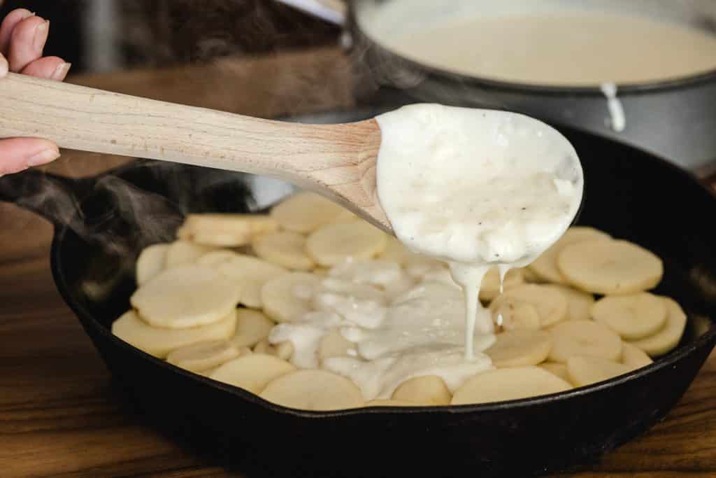 Cheese sauce being drizzled on top of sliced potatoes.