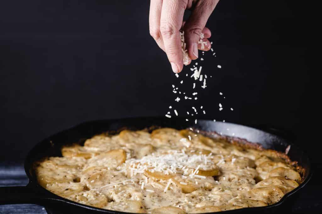 Cheese being sprinkled on smoked scalloped potatoes.