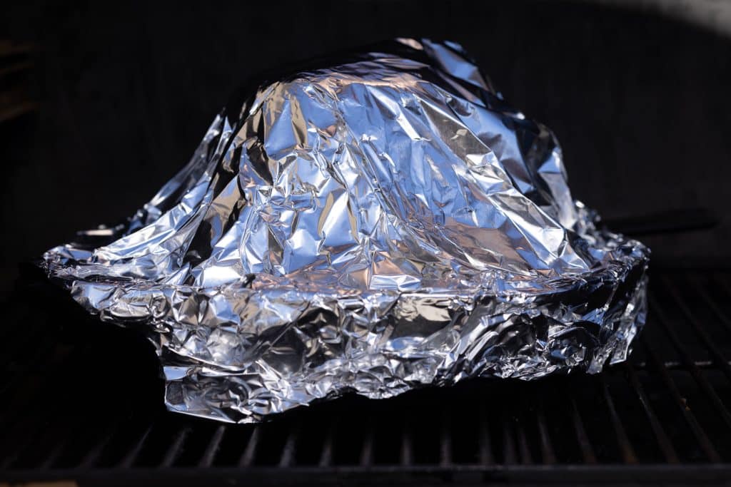 Spiral ham topped with aluminum foil on a smoker.