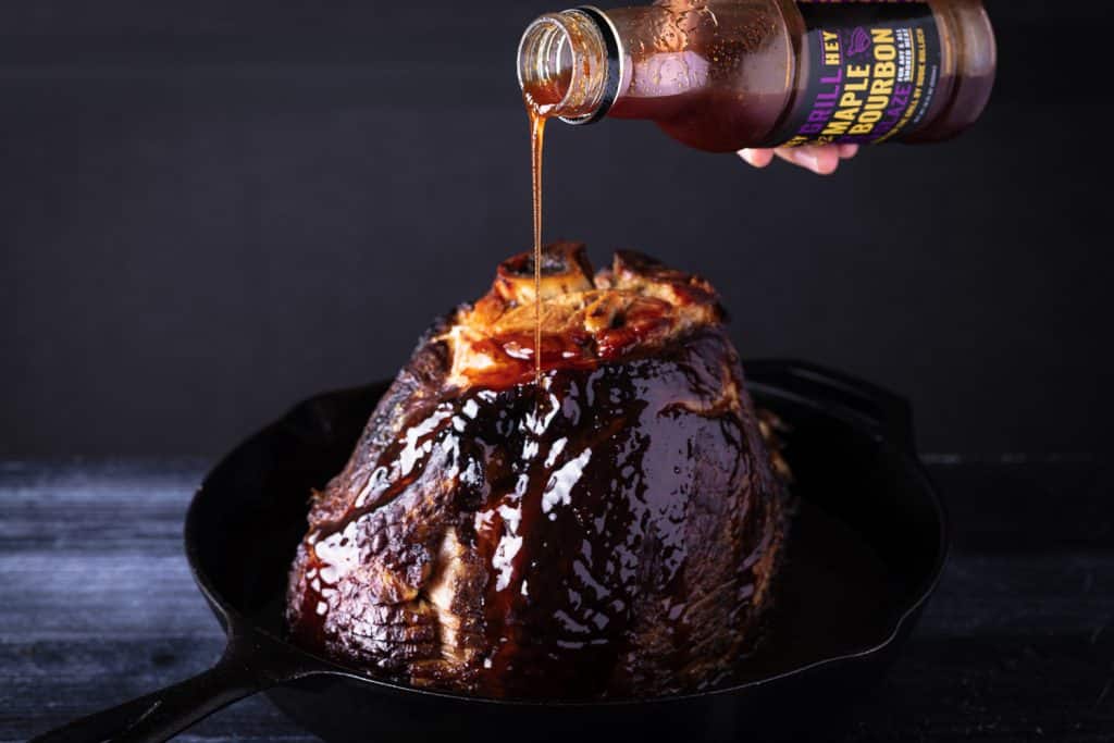 Maple bourbon glaze being drizzled on top of a smoked spiral ham.