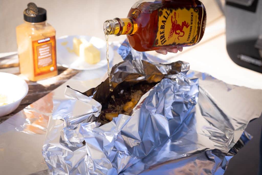 Fireball whiskey being poured onto ribs in a foil packet.