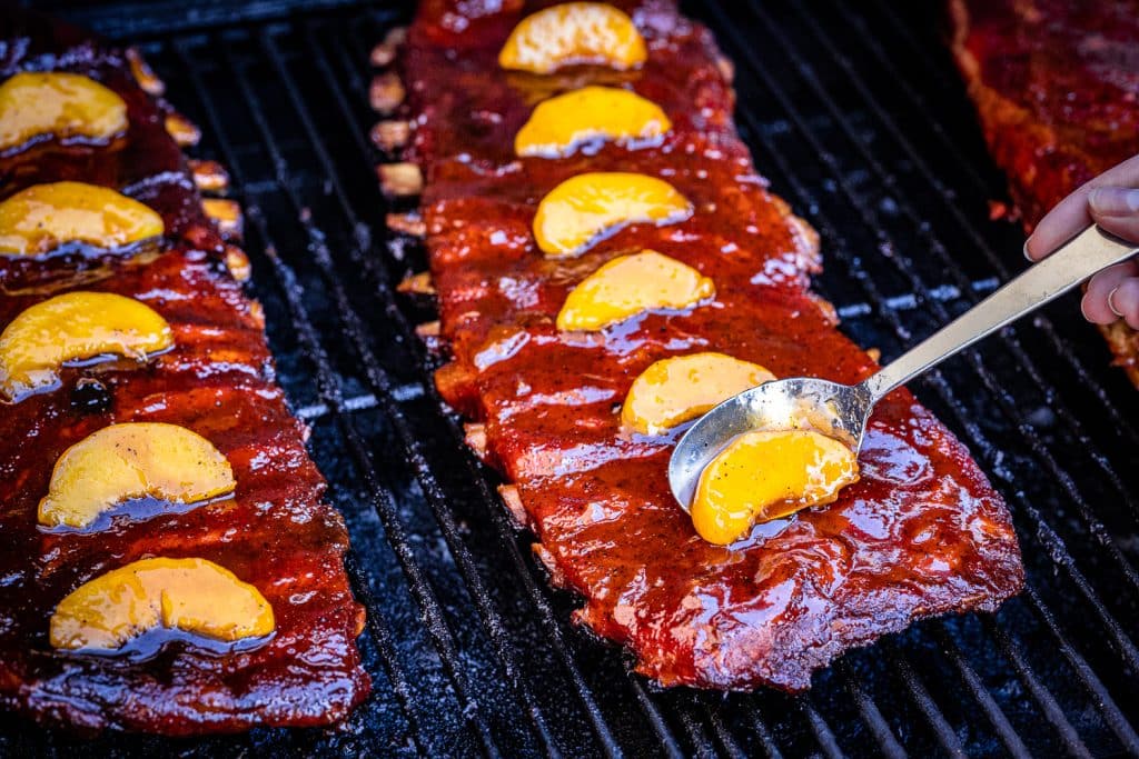 Peach slices being spooned onto fireball smoked ribs.