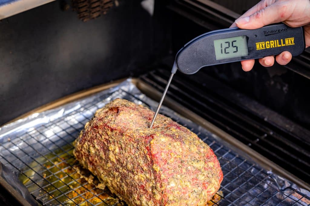 Instant-read thermometer showing 125 degrees F in a smoked bottom round roast.