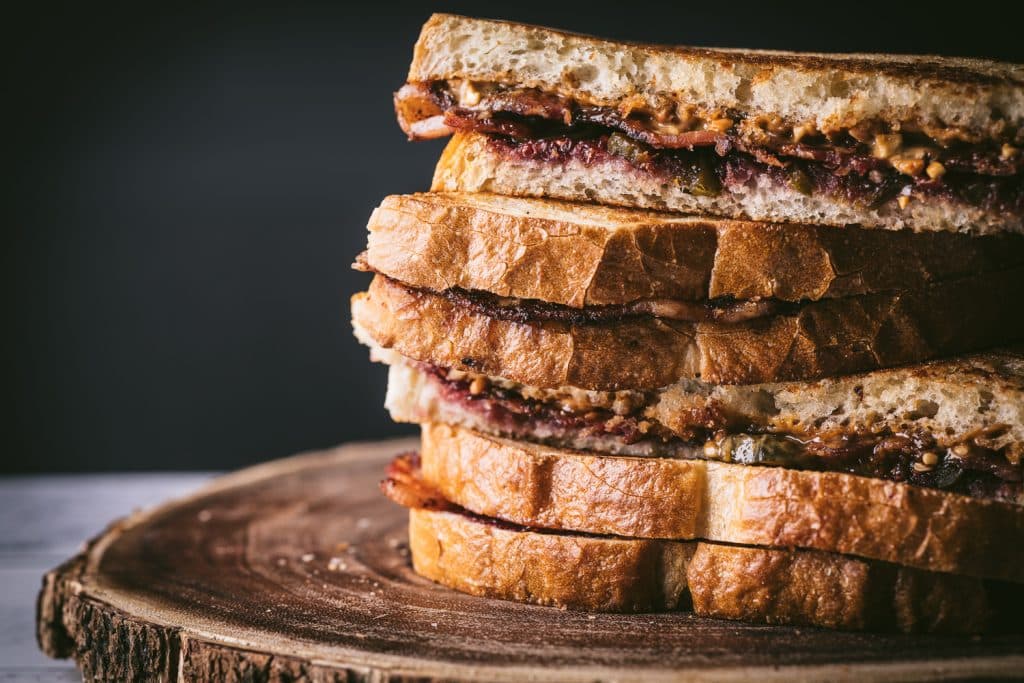 Peanut butter and jelly sandwiches stacked on a wooden serving dish.