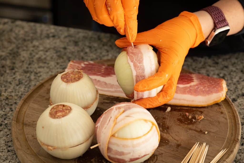 Bacon being attached to an onion bomb with toothpicks.