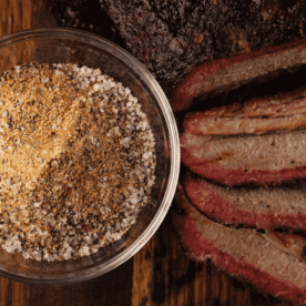 Brisket rub in a small bowl next to smoked beef brisket.