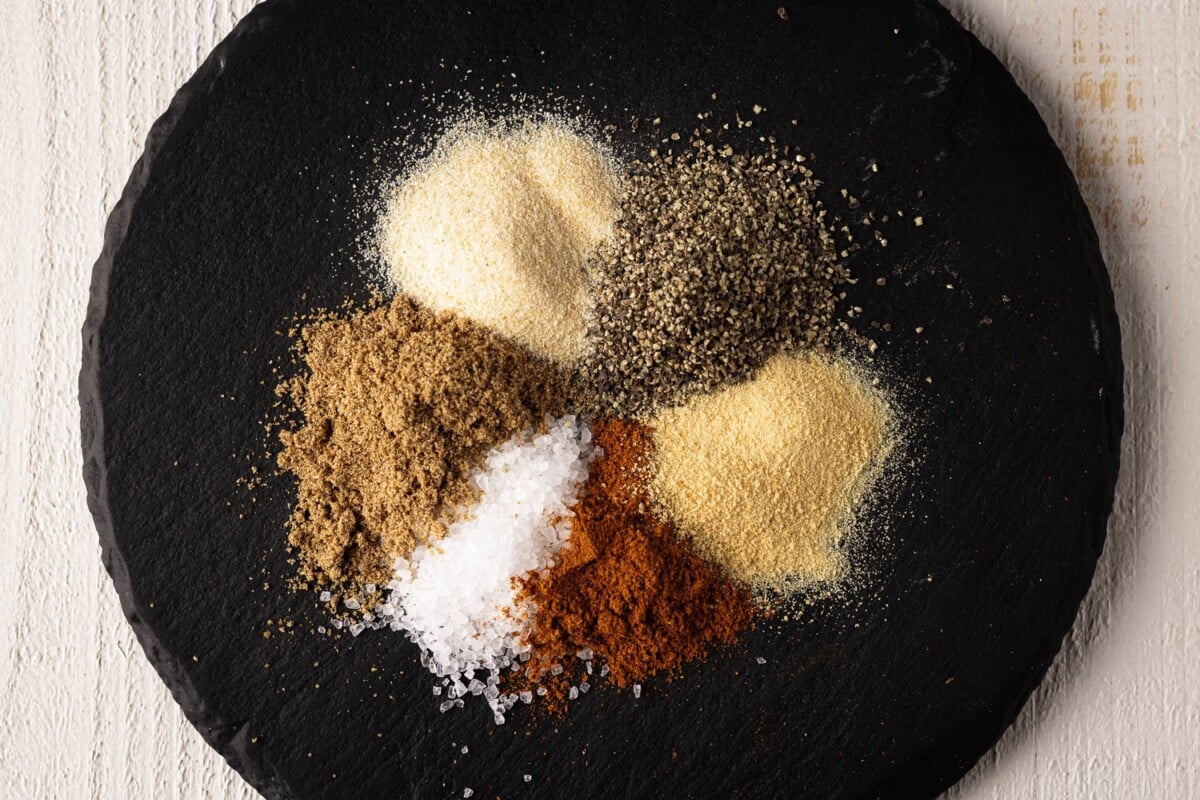 Six dry seasoning ingredients on a black plate.