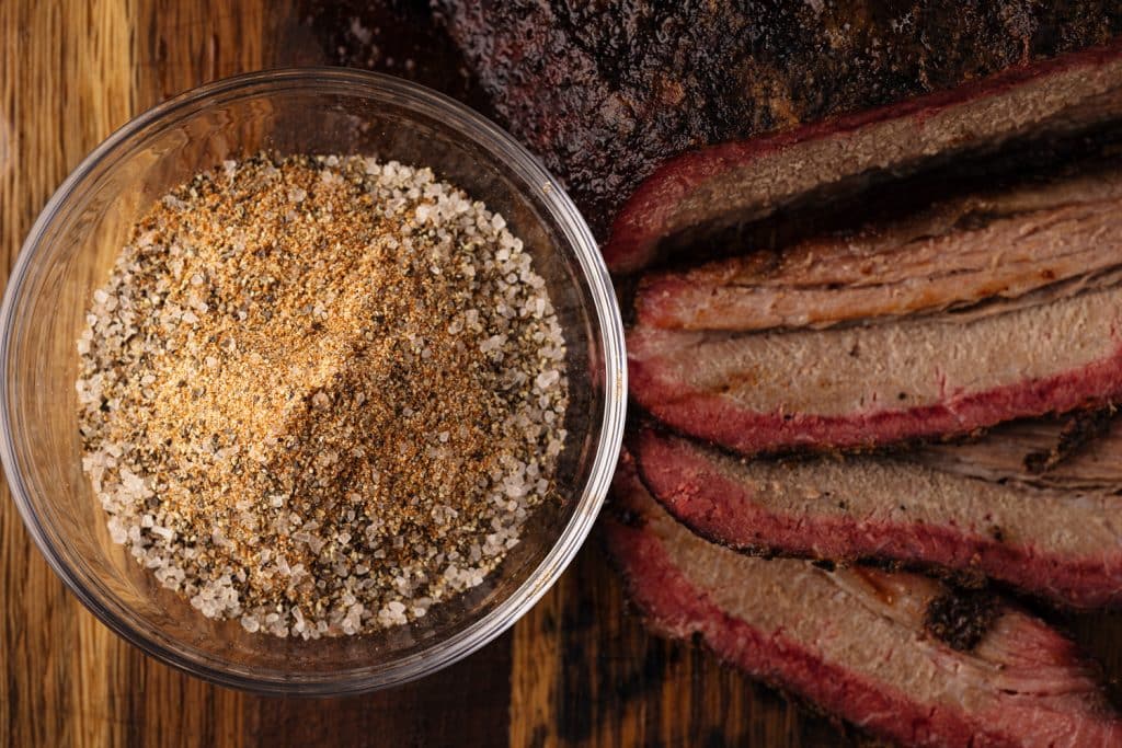 Brisket rub in a small bowl next to smoked beef brisket.