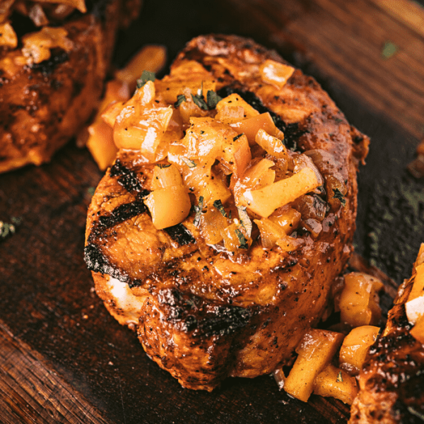 Pork loin chop topped with grilled apples and onions on a wooden cutting board.