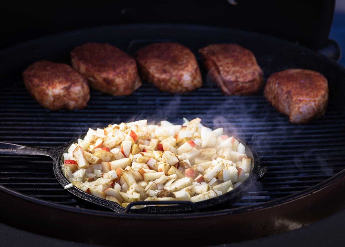 Chipped apples in a cat-iron skillet on the grill next to BBQ pork.