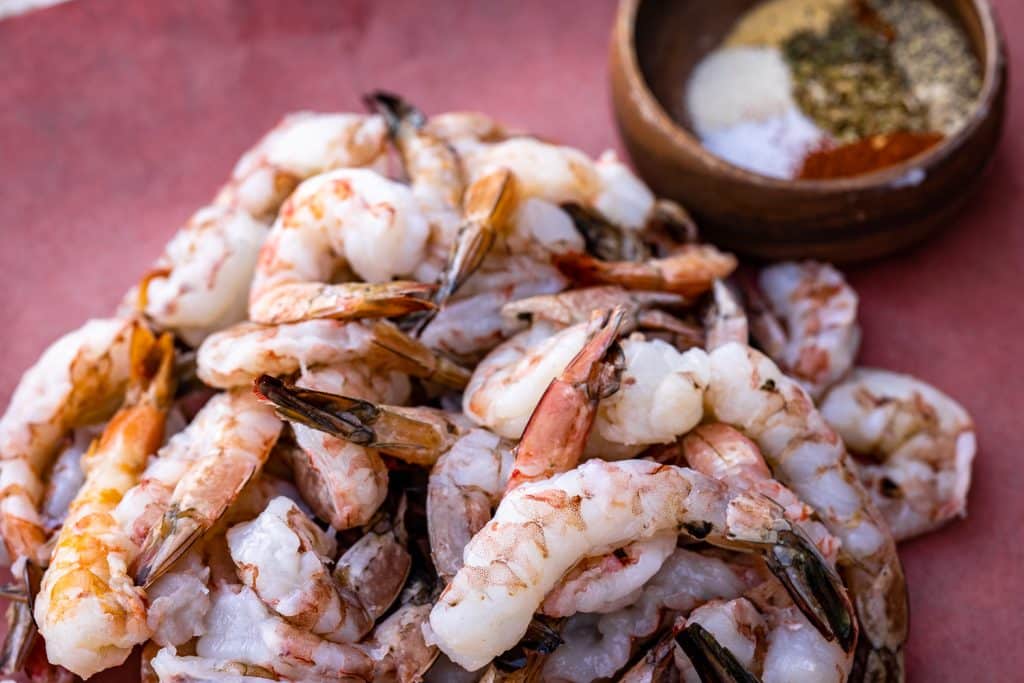 Pile of shrimp next to a bowl of blackened seasoning.