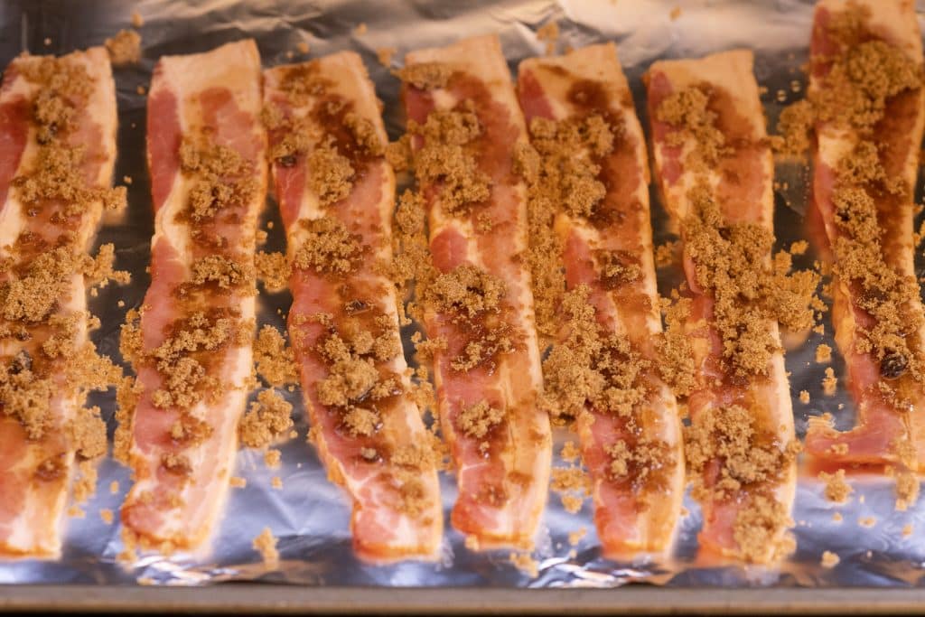 Bacon sprinkled with brown sugar on a sheet of aluminum foil.