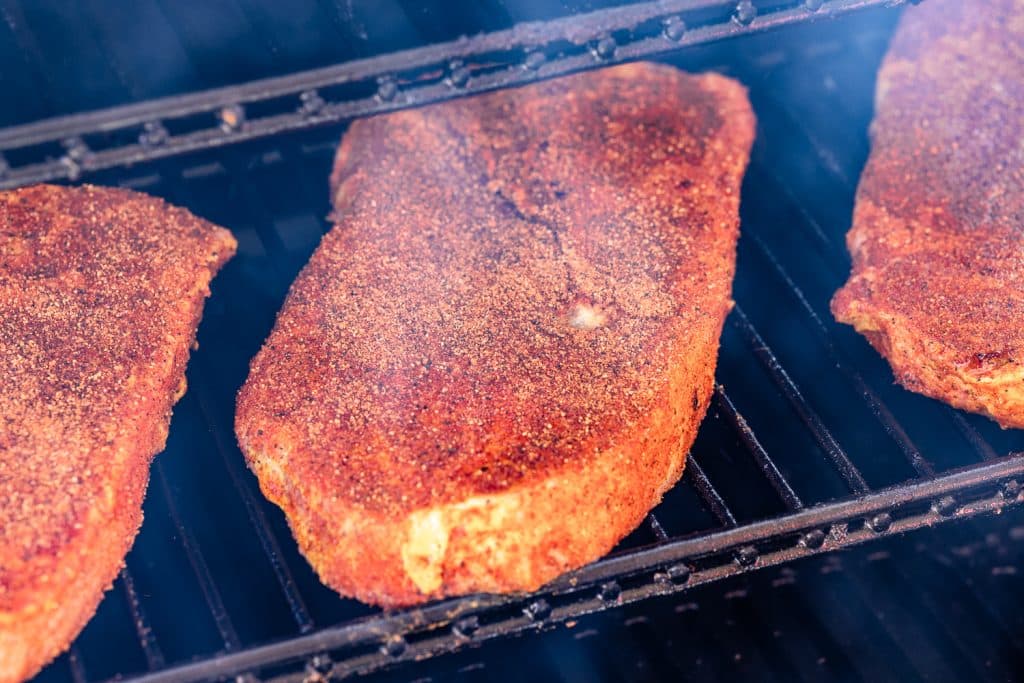 Seasoned pork steaks on the grill grates of a smoker.