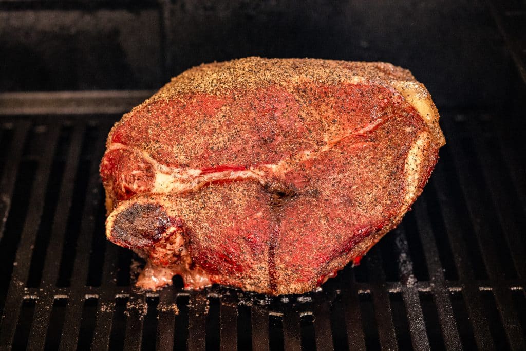 Seasoned lamb shoulder on the grill grates of a smoker.