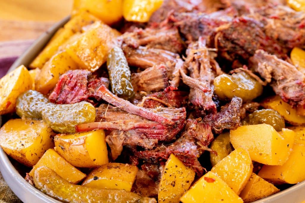 Smoked dill pickle pot roast surrounded by pickles and potatoes.