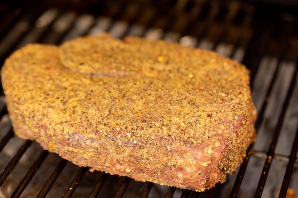 Seasoned chuck roast on the grill grates of a smoker.