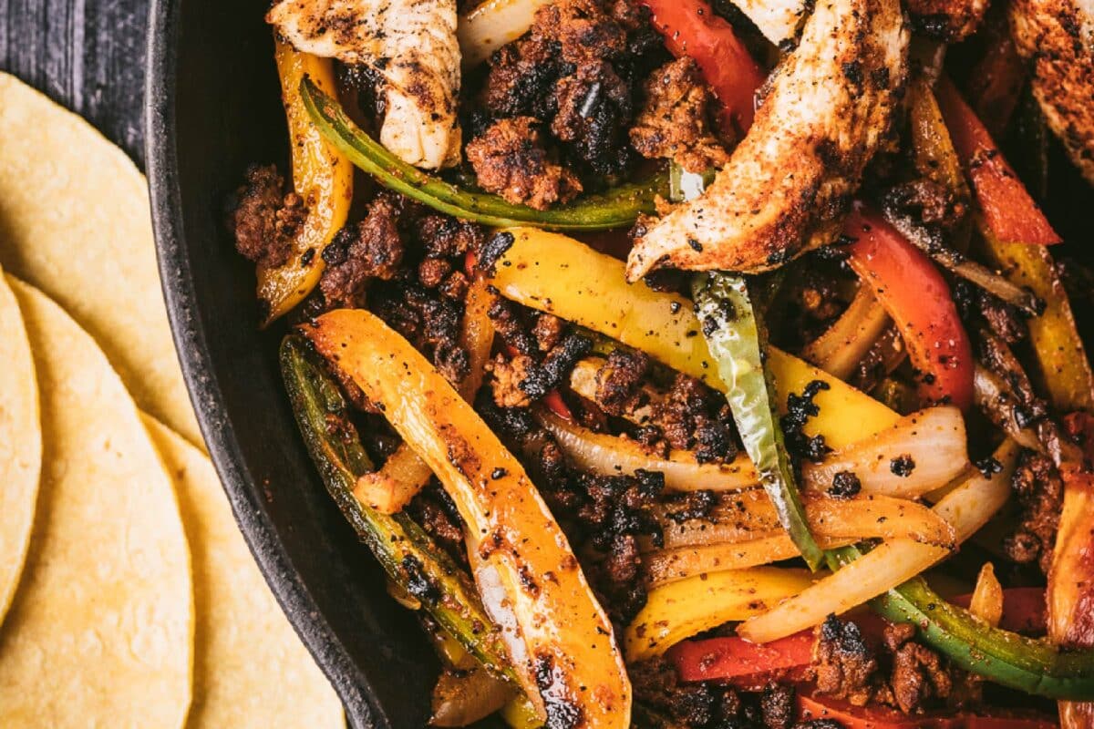 A skillet filled with chicken and peppers next to a pile of tortillas.