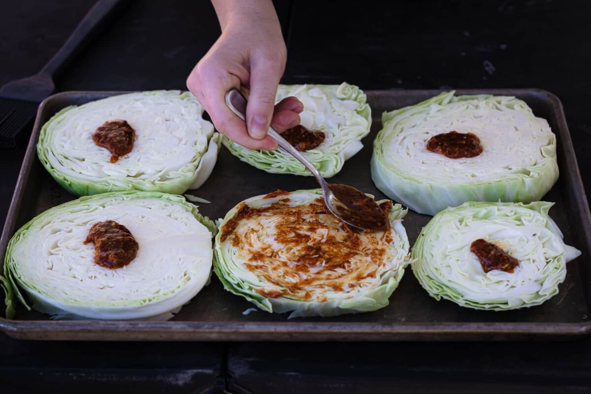 Lettuce head slices on a baking sheet being drizzled with BBQ sauce.