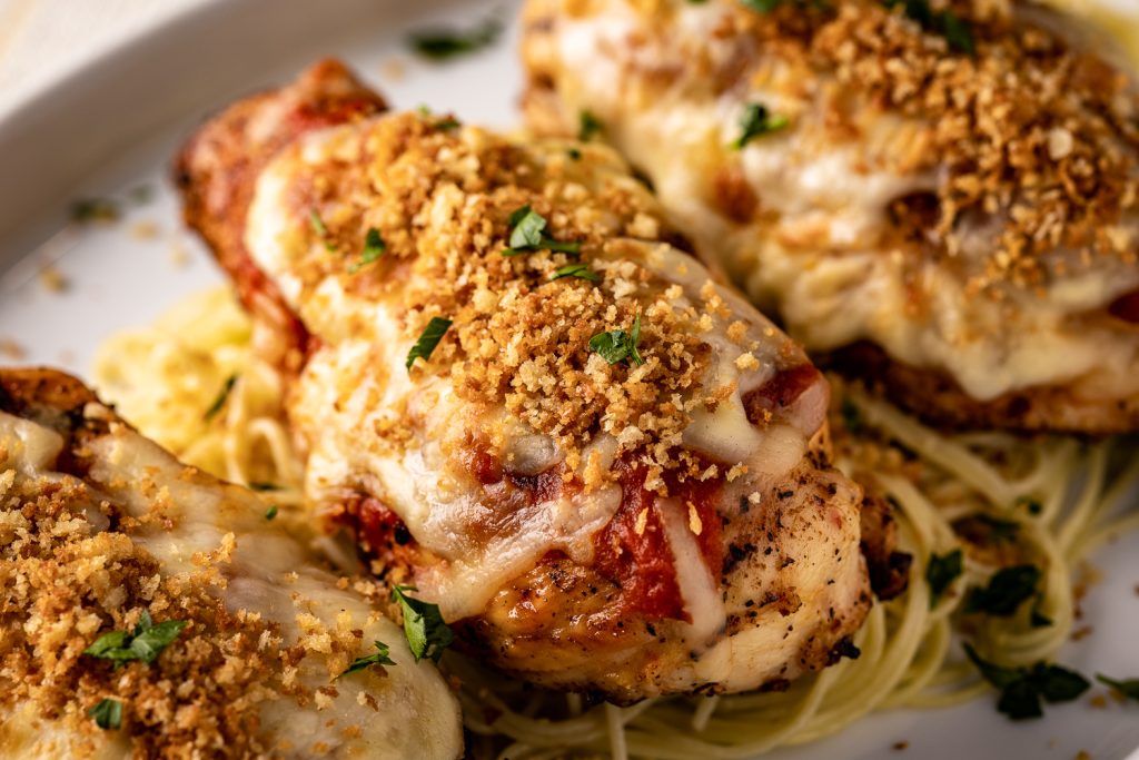 Grilled chicken parmesan topped with Panko on a white plate.