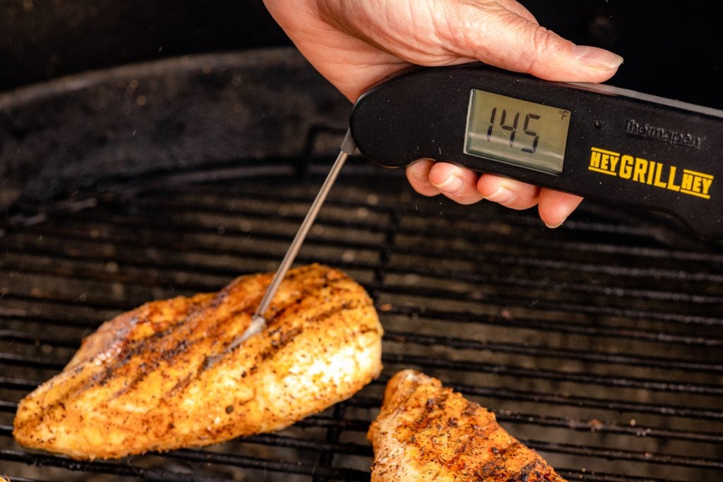Seasoned chicken breast on the grill with an instant read thermometer in one reading 145 degrees F.