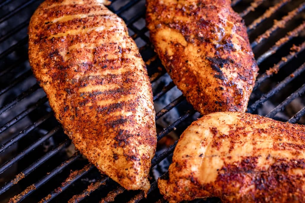 Three seasoned chicken breasts on the grill.