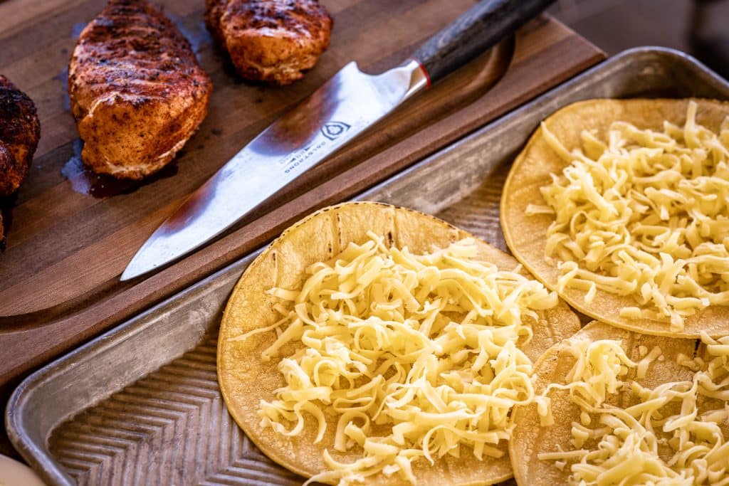 Chicken breasts next to tortillas covered in shredded cheese.
