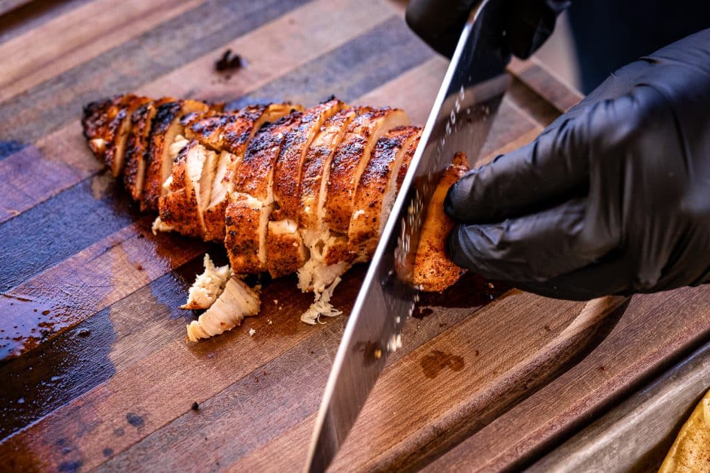 BBQ chicken being sliced on a wooden cutting board.
